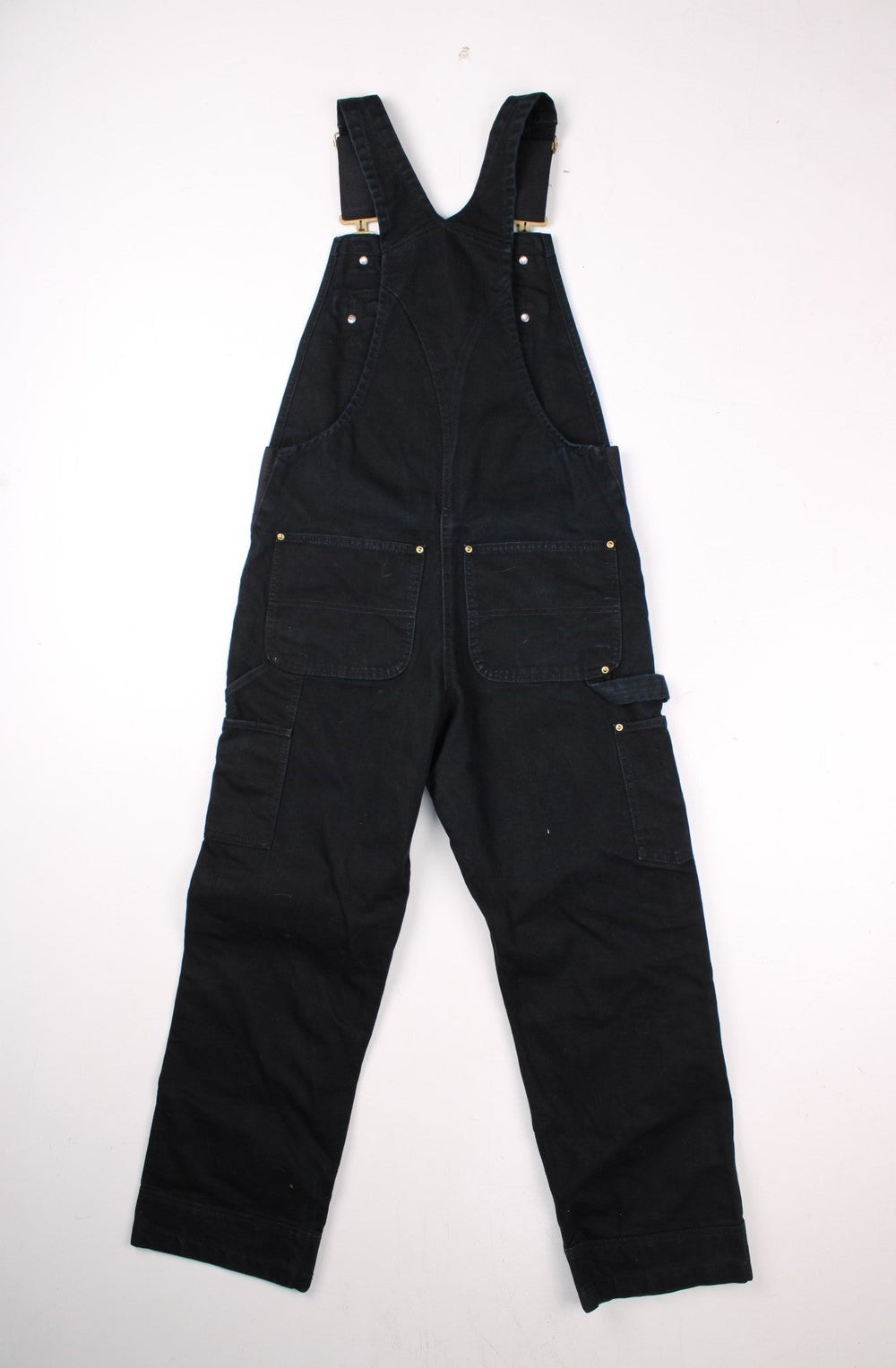 Carhartt dungarees in black with multiple pockets, elasticated straps, elastic panels at the waist, and a white logo patch on the front. .