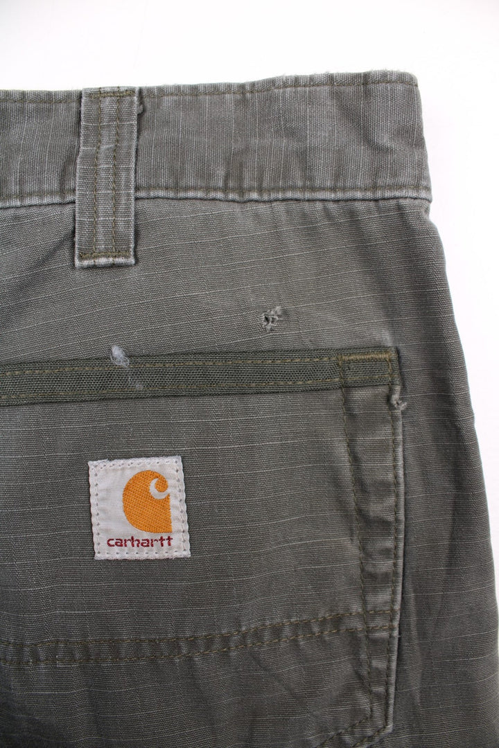 Carhartt cargo trousers in khaki green with multiple pockets, zip and button closure, and a logo patch on the back pocket.