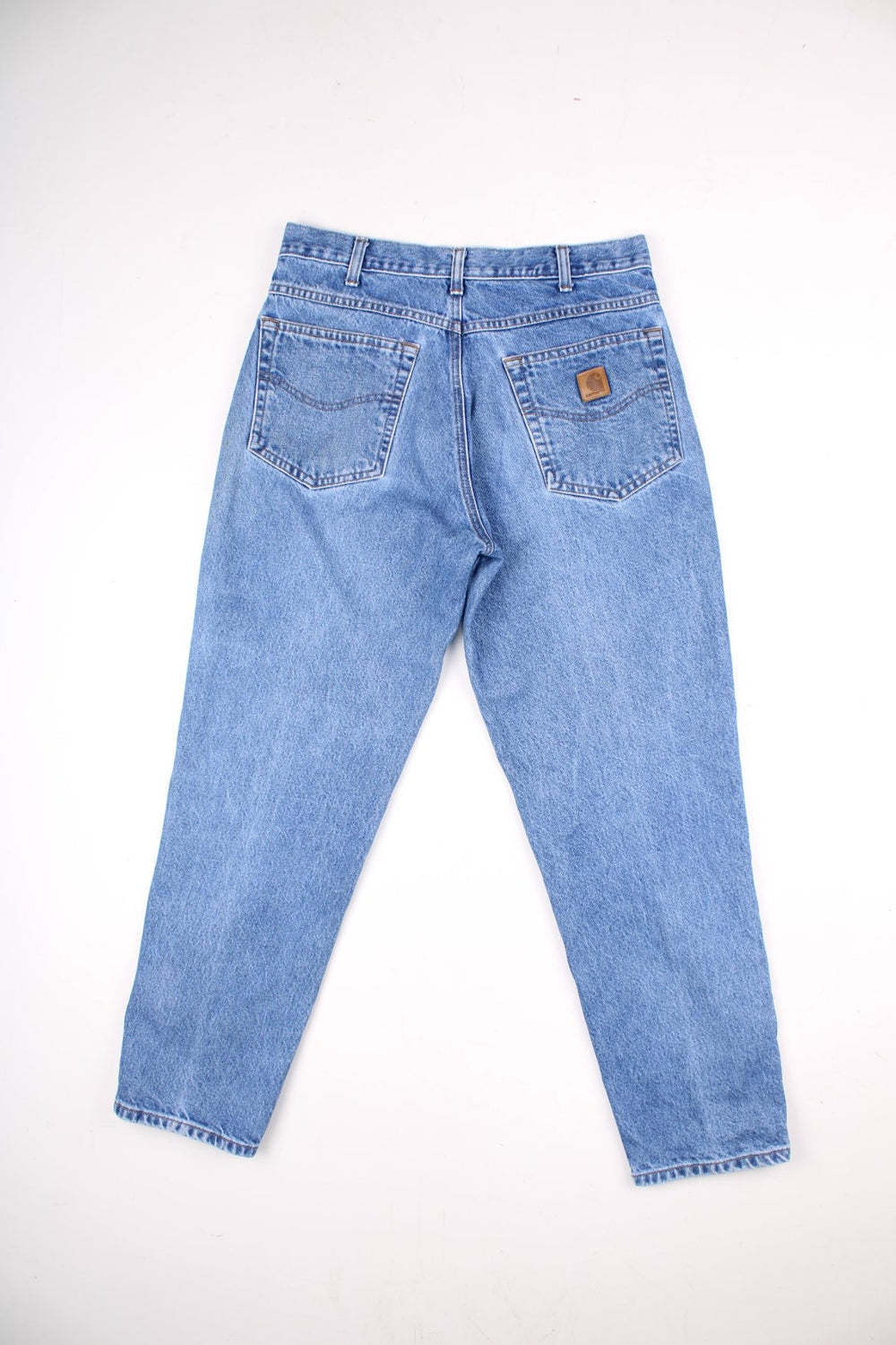 Carhartt jeans in a light blue wash with multiple pockets, zip and button closure, and a leather logo patch on the back pocket.