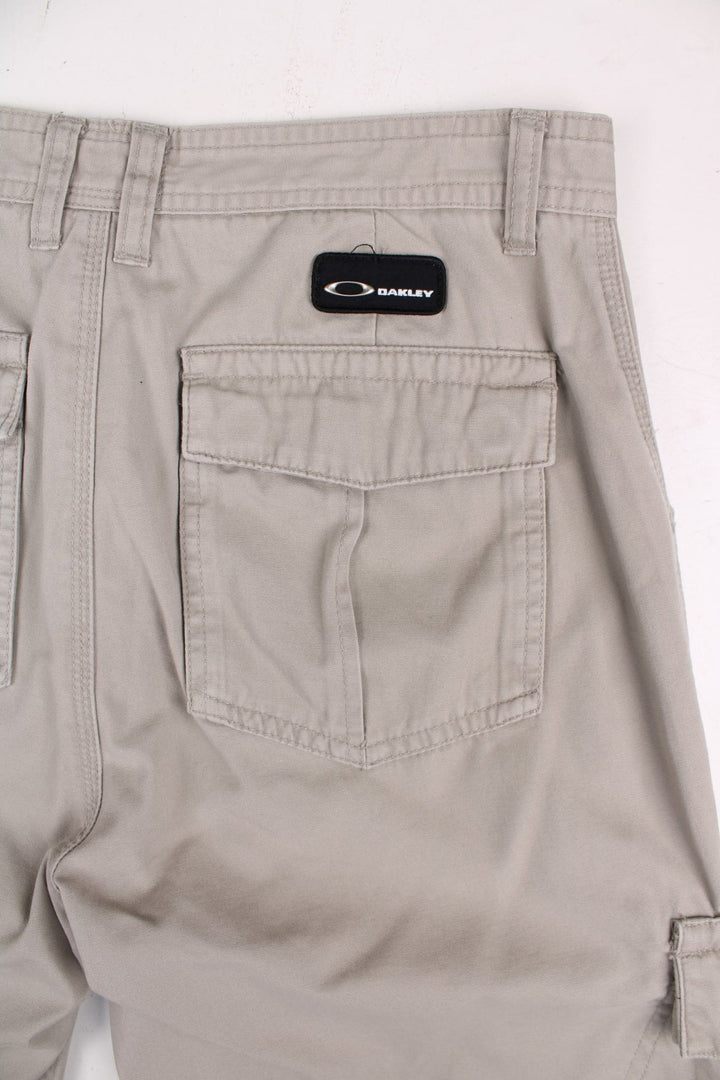 Oakley cargo trousers in tan with multiple pockets, zip and button closure, and a logo patch on the back.