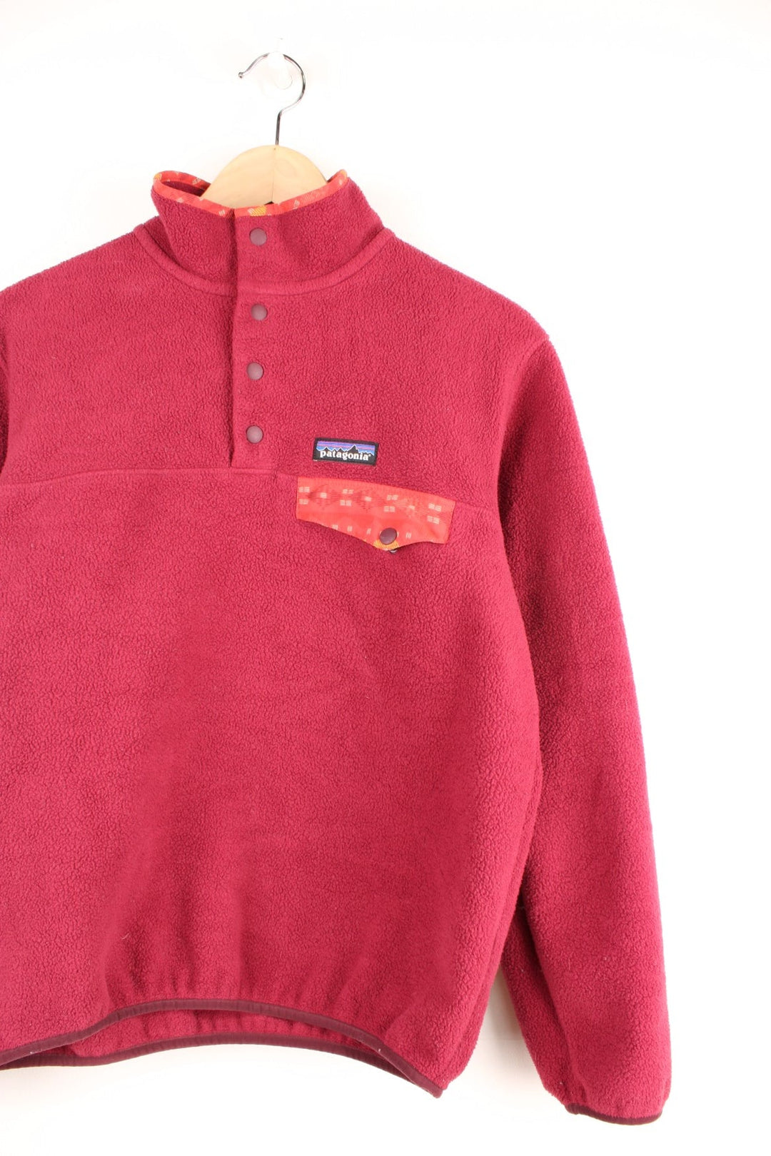 Dark Pink Patagonia Synchilla fleece with 1/4 snap closure, a breast pocket, red patterned detailing on the collar, and an embroidered logo patch.  