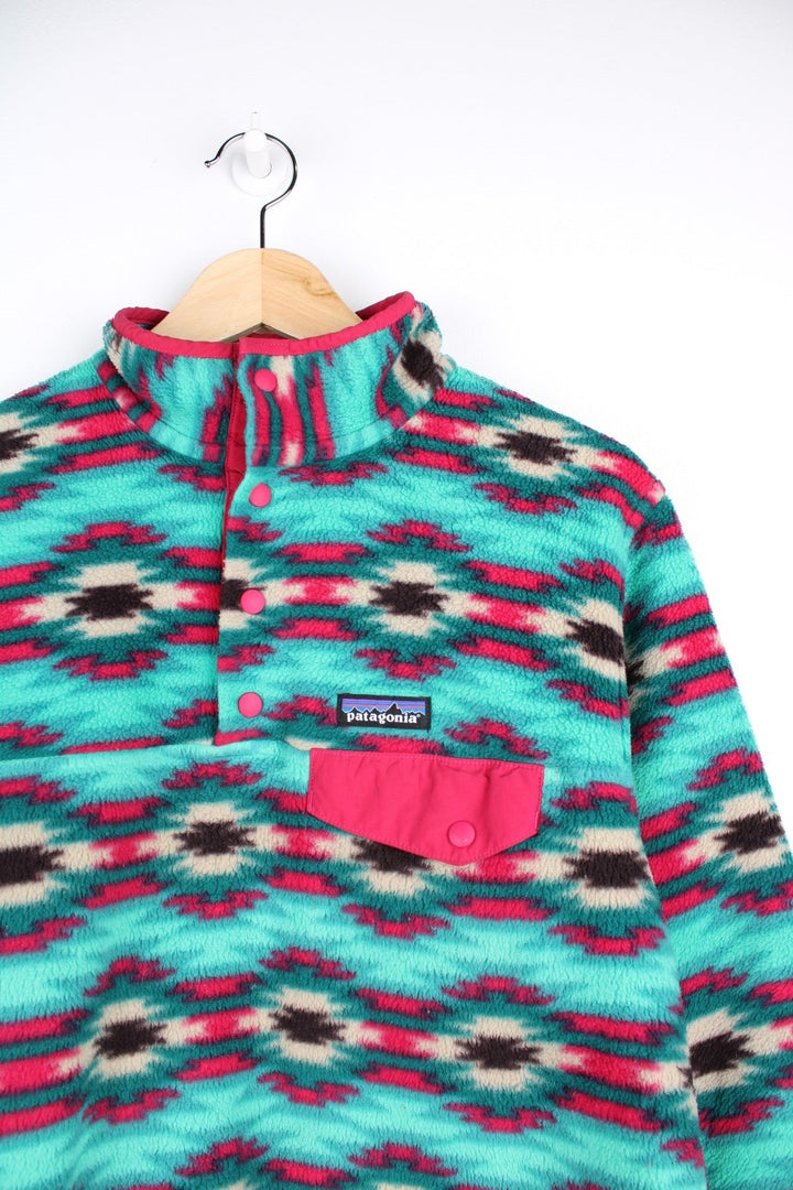 Patagonia fleece in a turquoise blue, pink, and purple pattern with 1/4 snap closure, three pockets, and a small logo on the chest.