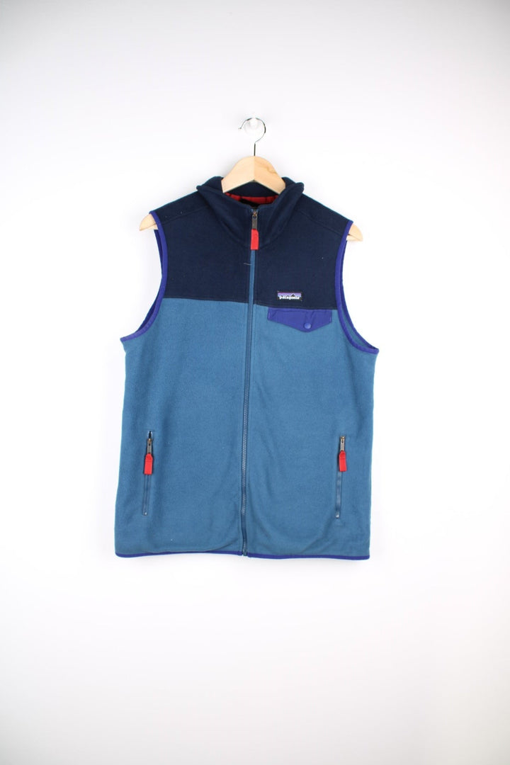 Patagonia fleece gilet in blue with darker blue top half and piping, zip closure and pockets with red zip toggles, and a small logo on the chest.