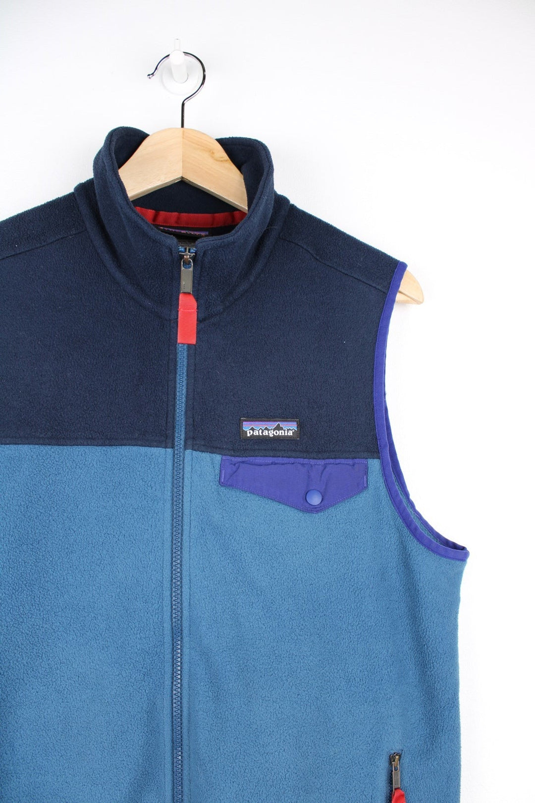 Patagonia fleece gilet in blue with darker blue top half and piping, zip closure and pockets with red zip toggles, and a small logo on the chest.