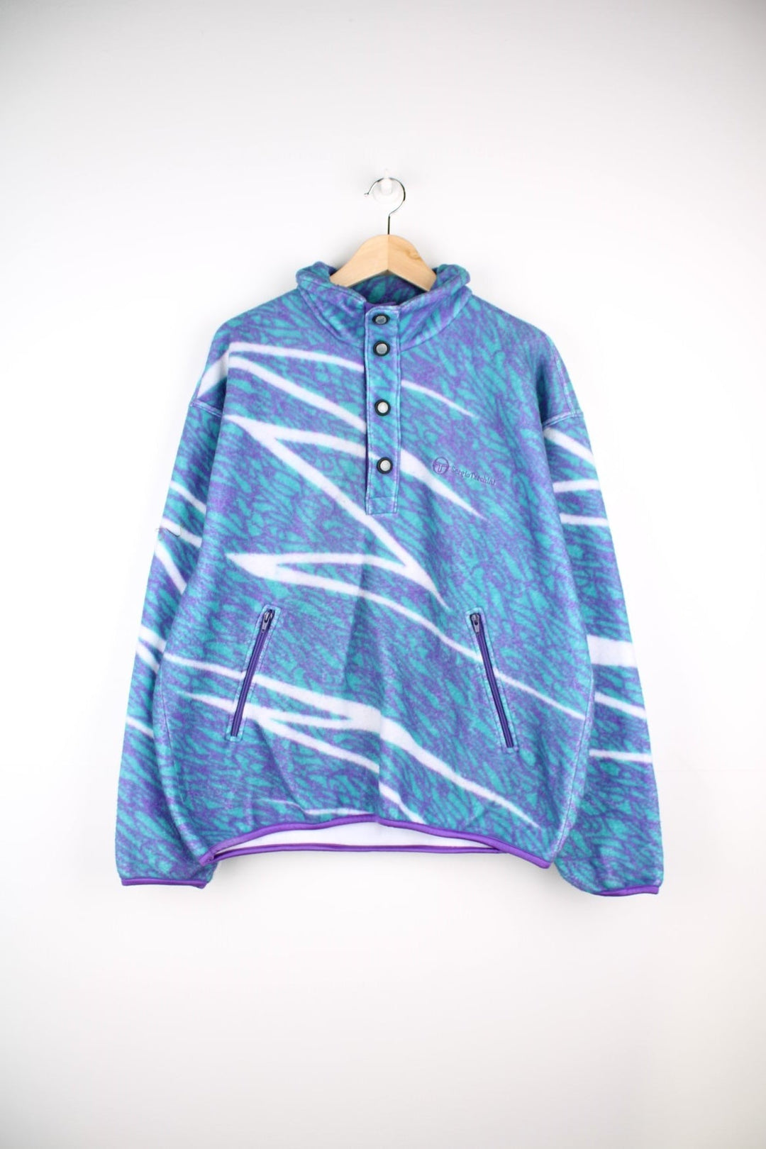 Sergio Tacchini fleece in a turquoise blue, purple, and white abstract squiggle pattern, with 1/2 snap closure, 2 zipped pockets and an embroidered logo on the chest.