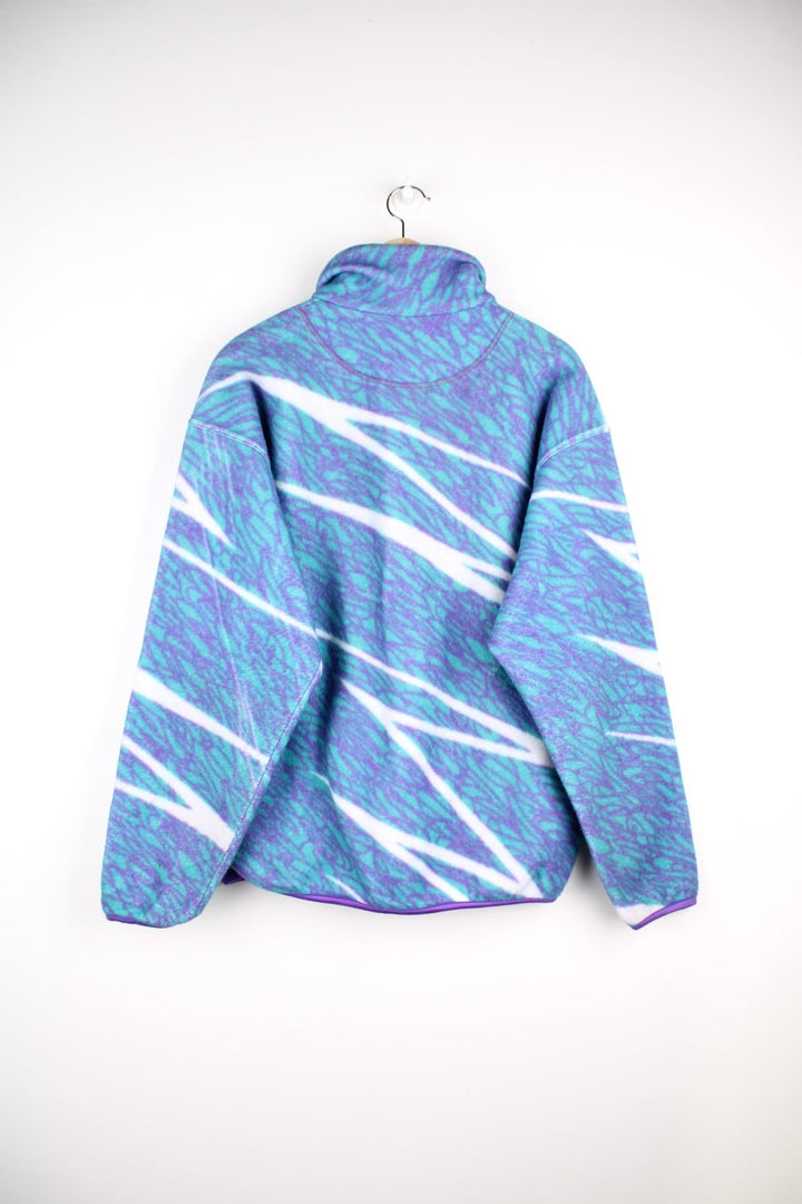 Sergio Tacchini fleece in a turquoise blue, purple, and white abstract squiggle pattern, with 1/2 snap closure, 2 zipped pockets and an embroidered logo on the chest.