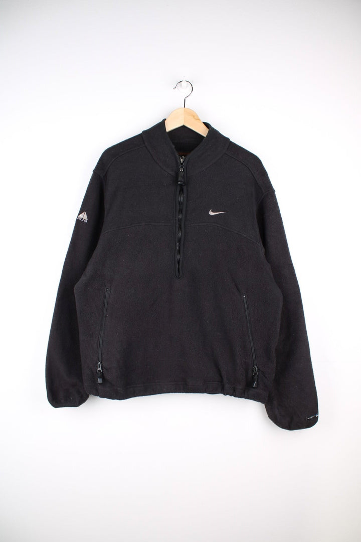 Nike ACG 1/2 zip fleece in black with two zipped pockets, Nike swoosh and ACG logos embroidered on the chest and sleeve respectively, a 'Nike Fit' patch on the cuff and 'All COnditions Gear' patch on the back.