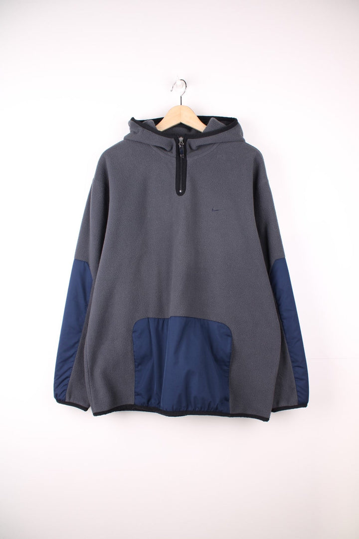 Dark grey Nike fleece quarter zip hoodie with navy blue contrast front pocket and sleeve panels, an embroideres swoosh logo on the front, and Nike spellout embroidered on the back. 