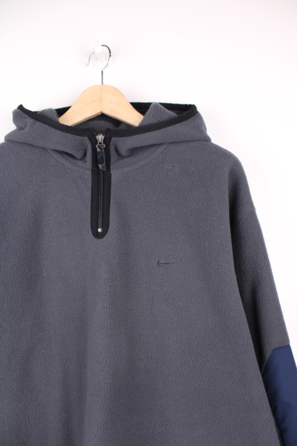 Dark grey Nike fleece quarter zip hoodie with navy blue contrast front pocket and sleeve panels, an embroideres swoosh logo on the front, and Nike spellout embroidered on the back. 