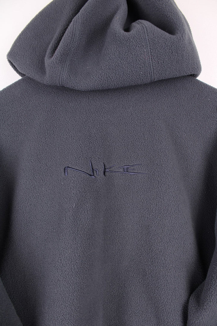 Dark grey Nike fleece quarter zip hoodie with navy blue contrast front pocket and sleeve panels, an embroideres swoosh logo on the front, and Nike spellout embroidered on the back. 