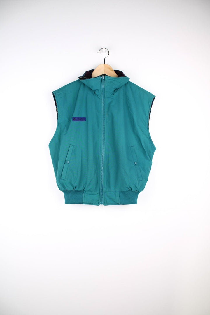 Columbia zip-through reversible fleece gilet in a blue, green, and purple geometric pattern. The reverse side is a turquoise water-resistant material. Both have pockets and a logo patch on the chest. 