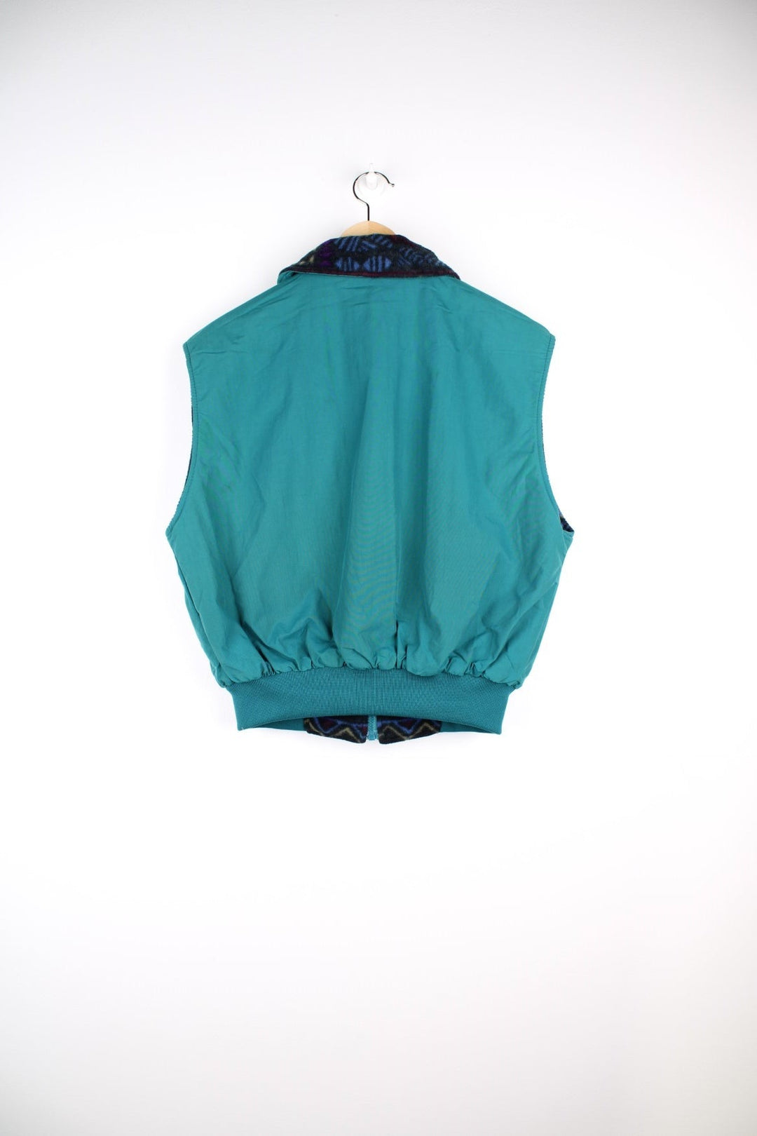 Columbia zip-through reversible fleece gilet in a blue, green, and purple geometric pattern. The reverse side is a turquoise water-resistant material. Both have pockets and a logo patch on the chest. 