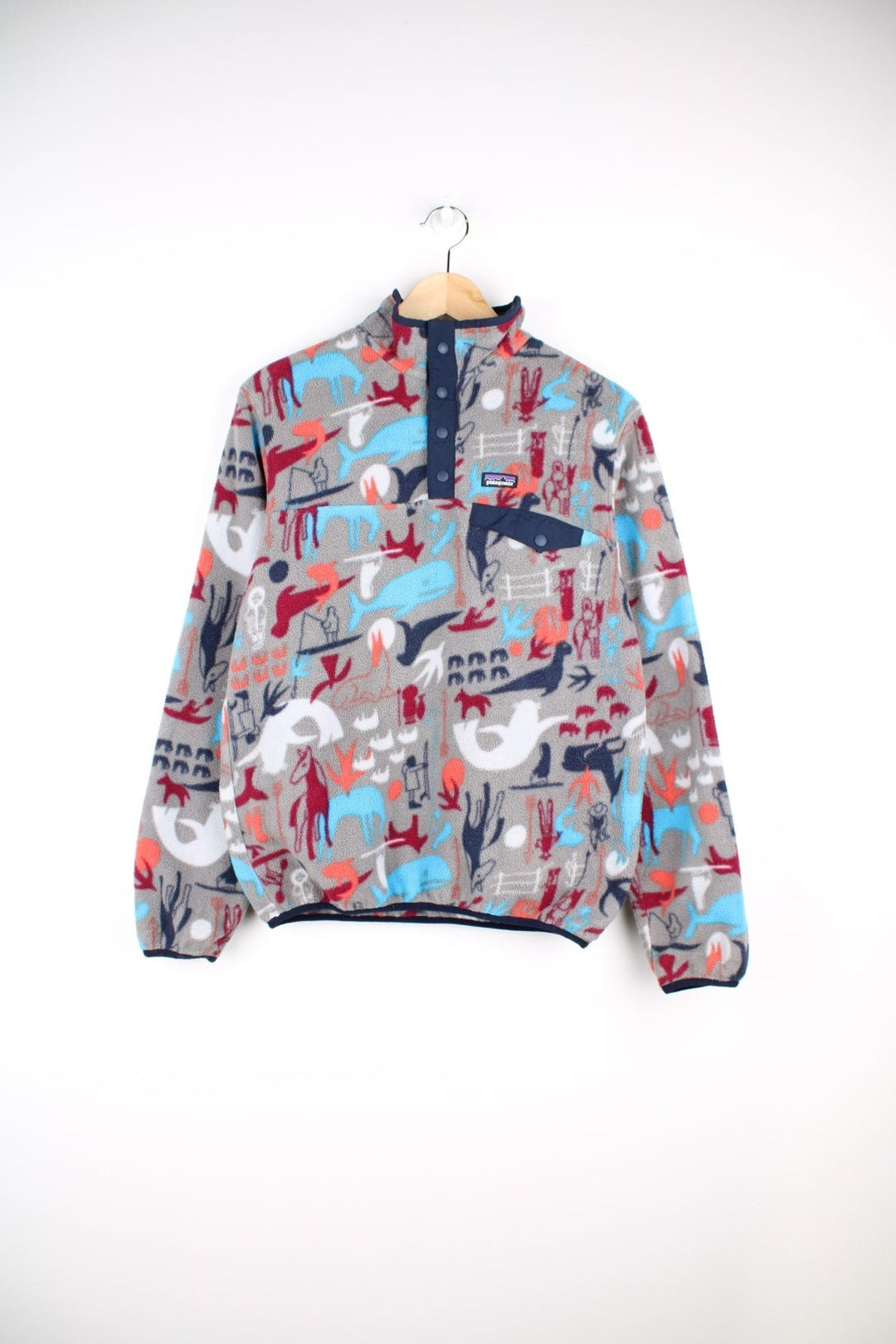 Patagonia fleece in grey with a print of cave painting animals in blue, red and orange, with 1/4 snap closure, one pocket and a small logo on the chest.