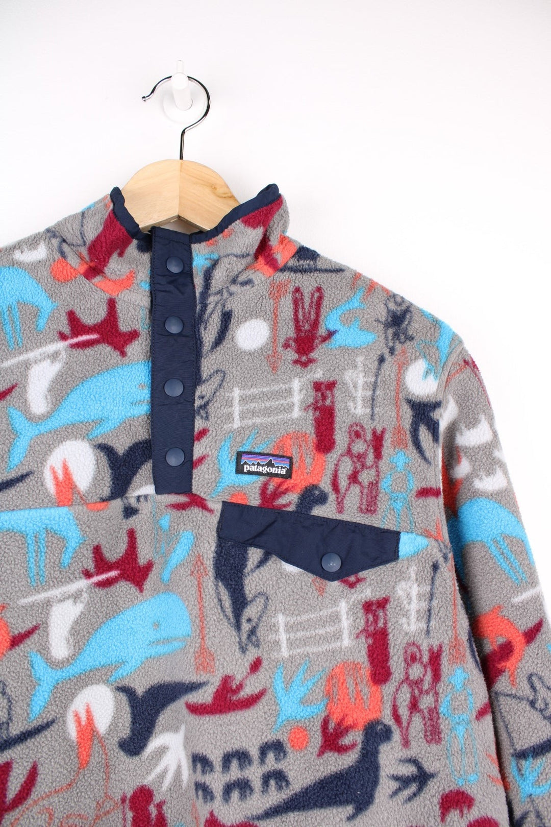 Patagonia fleece in grey with a print of cave painting animals in blue, red and orange, with 1/4 snap closure, one pocket and a small logo on the chest.