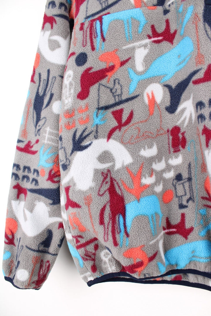 Patagonia fleece in grey with a print of cave painting animals in blue, red and orange, with 1/4 snap closure, one pocket and a small logo on the chest.