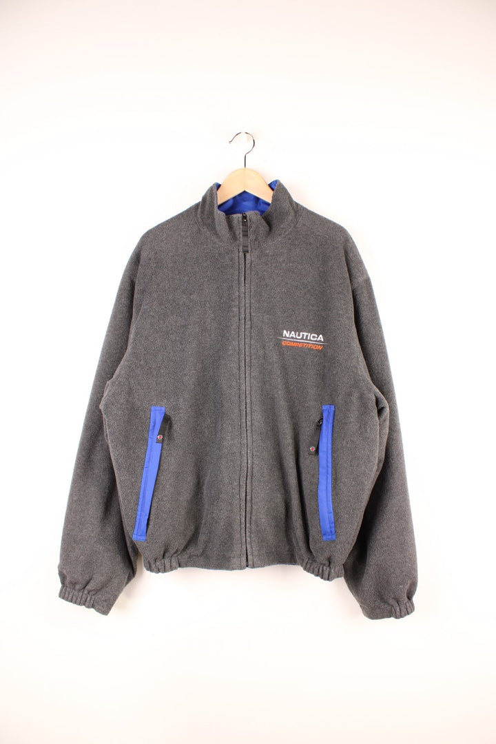 Grey Nautica reversible fleece jacket with a shower-proof side in blue and a fleece side in grey. Zipped pockets and embroidered logos on both sides. 