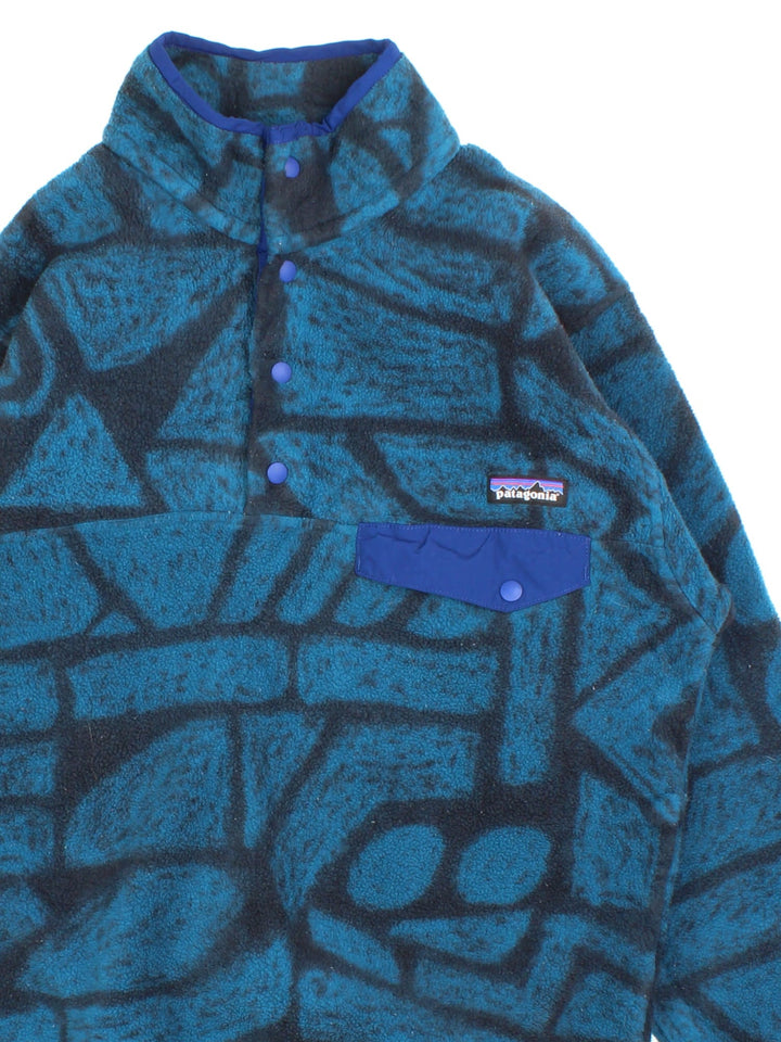 Patagonia Synchilla Fleece in a blue & black patterned colourway. 1/4 button up and small button pocket on the front with the small classic logo above. 