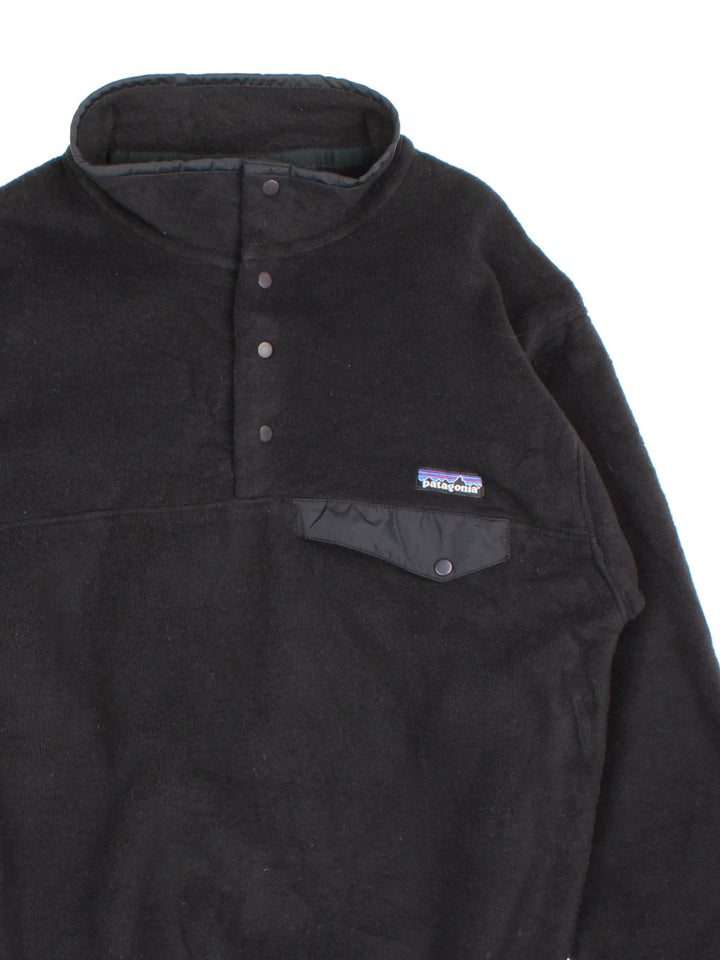 Patagonia Synchilla Fleece in a black colourway. 1/4 Buttons up and has button pocket on the front with the small classic logo above. 