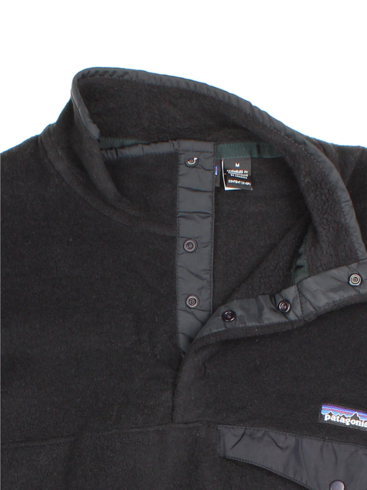 Patagonia Synchilla Fleece in a black colourway. 1/4 Buttons up and has button pocket on the front with the small classic logo above. 