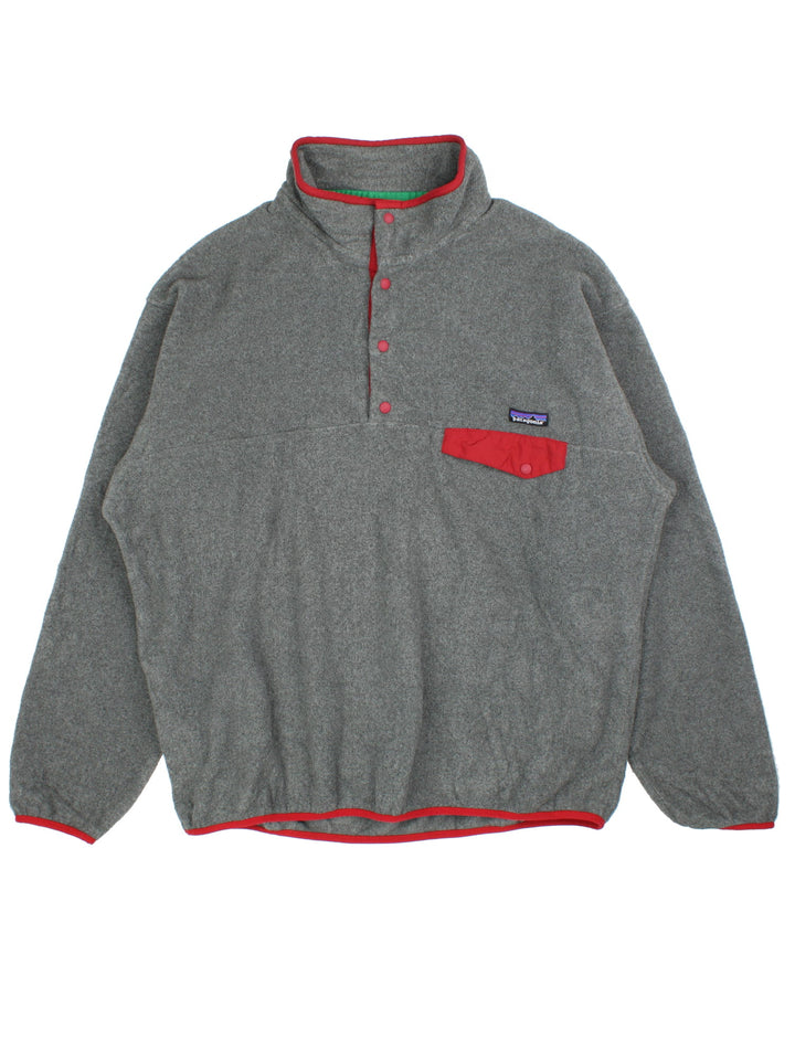 Patagonia Synchilla Fleece in a grey colourway with red trimming. 1/4 Buttons up and has button pocket on the front with the small classic logo above. 