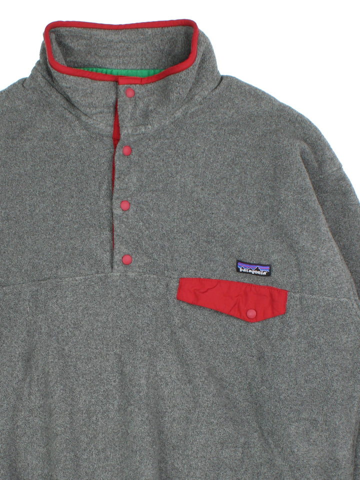 Patagonia Synchilla Fleece in a grey colourway with red trimming. 1/4 Buttons up and has button pocket on the front with the small classic logo above. 