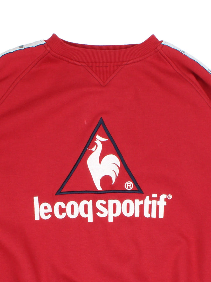 Vintage Le Coq Sportif Sweatshirt in a red colourway with large logo across the chest and stripe panelling with logo down the shoulder/sleeve.