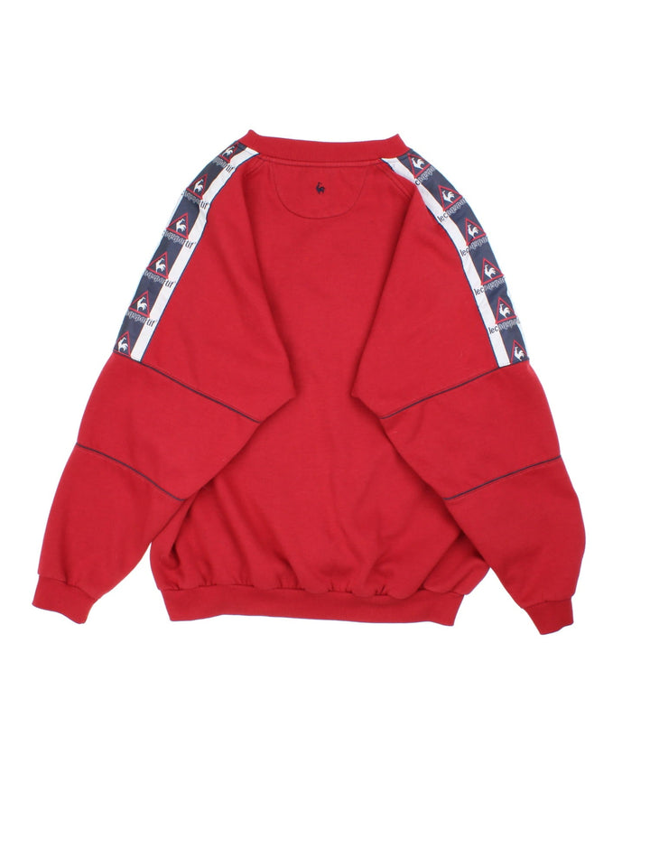 Vintage Le Coq Sportif Sweatshirt in a red colourway with large logo across the chest and stripe panelling with logo down the shoulder/sleeve.