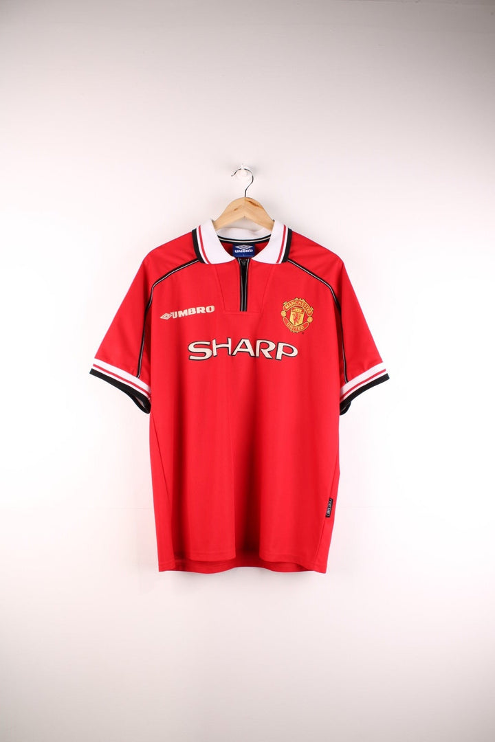 Manchester United 1998/99 Umbro Football Shirt in the red home kit colourway, features embroidered logos and badge on the front, zip up collar, and United number 1 printed on the back.