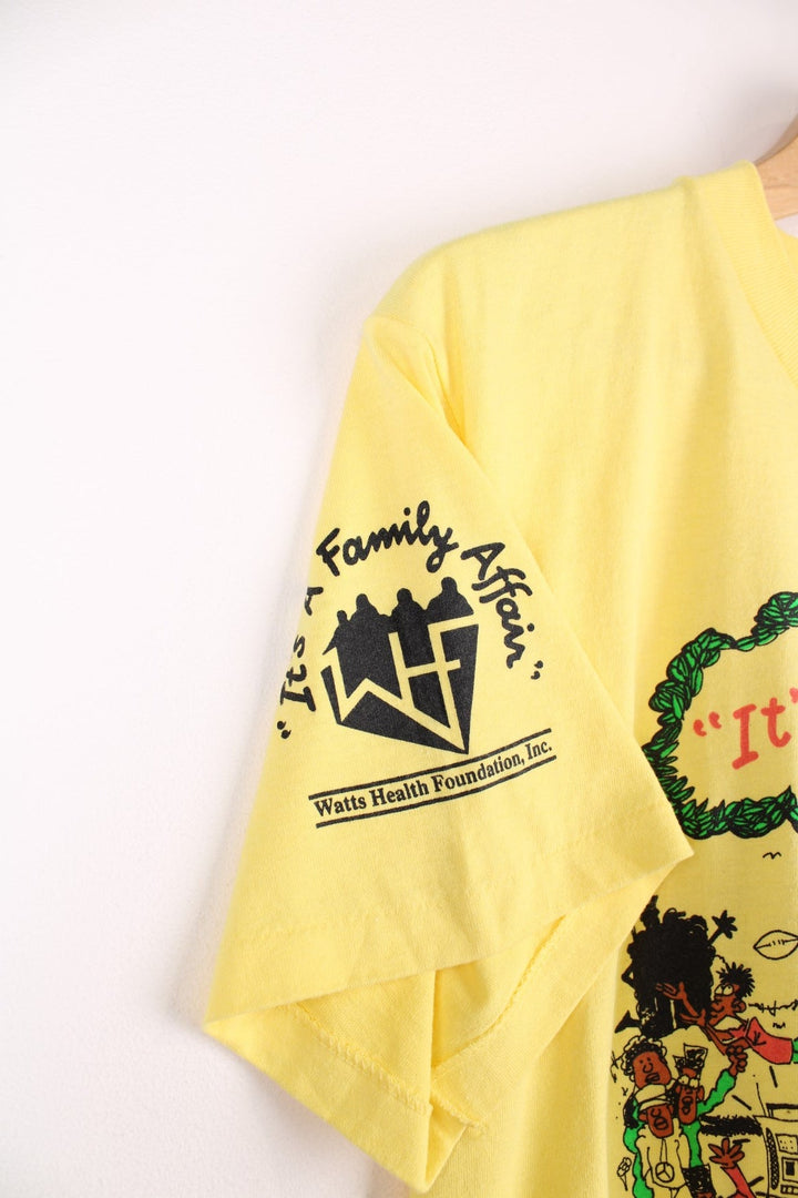 Vintage yellow graphic United Health Plan tee with cartoon design reading 'It's a Family Affair', and a Watts Health Foundation sponsorship logo on the right sleeve. 