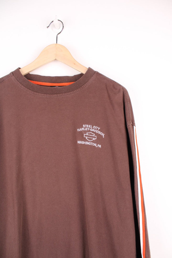 Harley Davidson Steel City, Washington, PA long sleeved top in brown. Features orange and white stripe down each sleeve, and embroidered spell out logo and eagle on the back. 