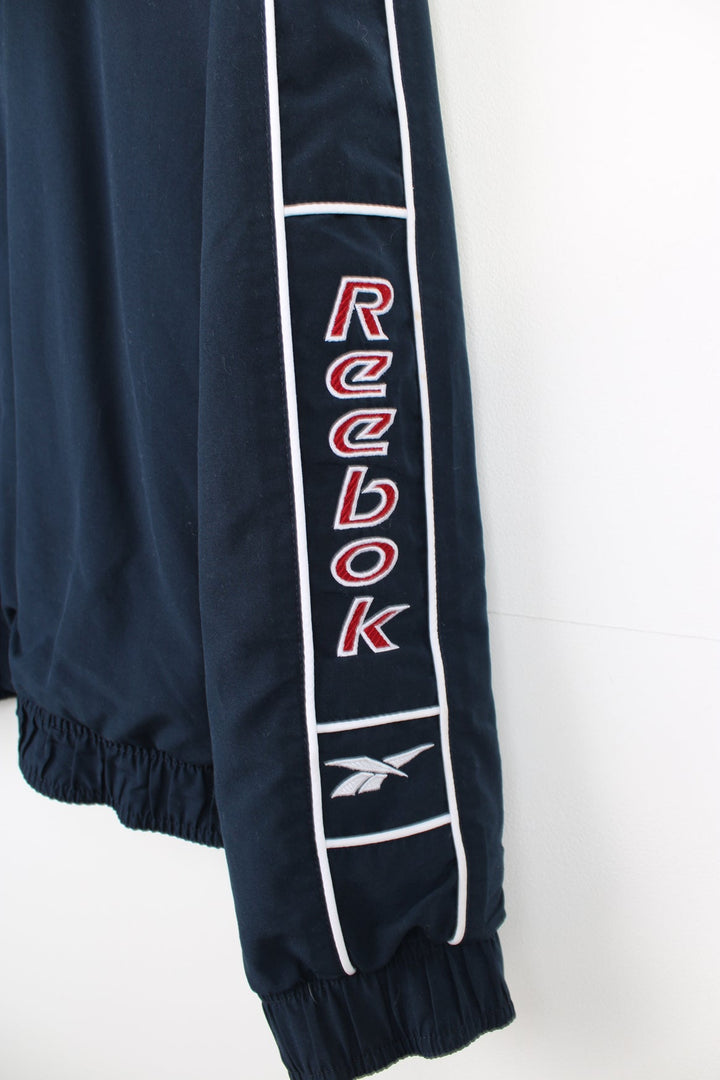 Vintage navy blue Reebok zip through track jacket with embroidered logo on the chest and spell-out down the sleeve