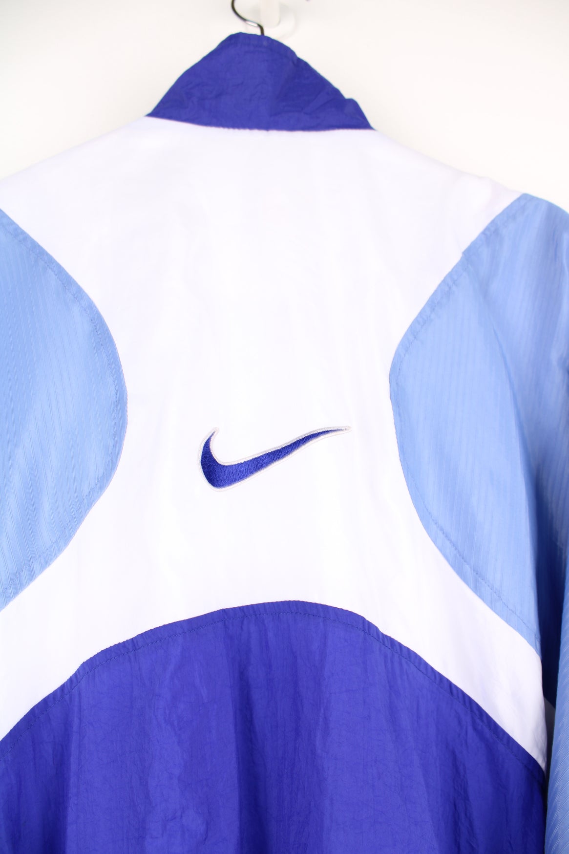 Nike Tracksuit Jacket in a blue and white patterned colourway, zip up with side pockets, and has the swoosh logo embroidered on the front and back.