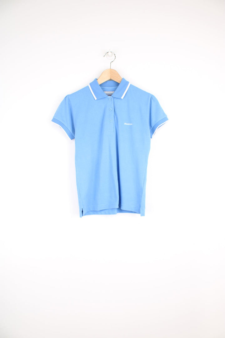 Vintage women's baby blue polo shirt by Reebok, features embroidered logo on the chest and white trim on the collar and sleeves