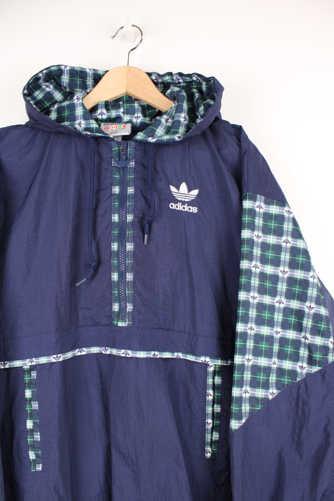 Adidas Pullover Windbreaker in a blue colourway with green and white tartan pattern throughout, hooded, half zip up, big pouch pocket, and has the logo embroidered on the front and back.