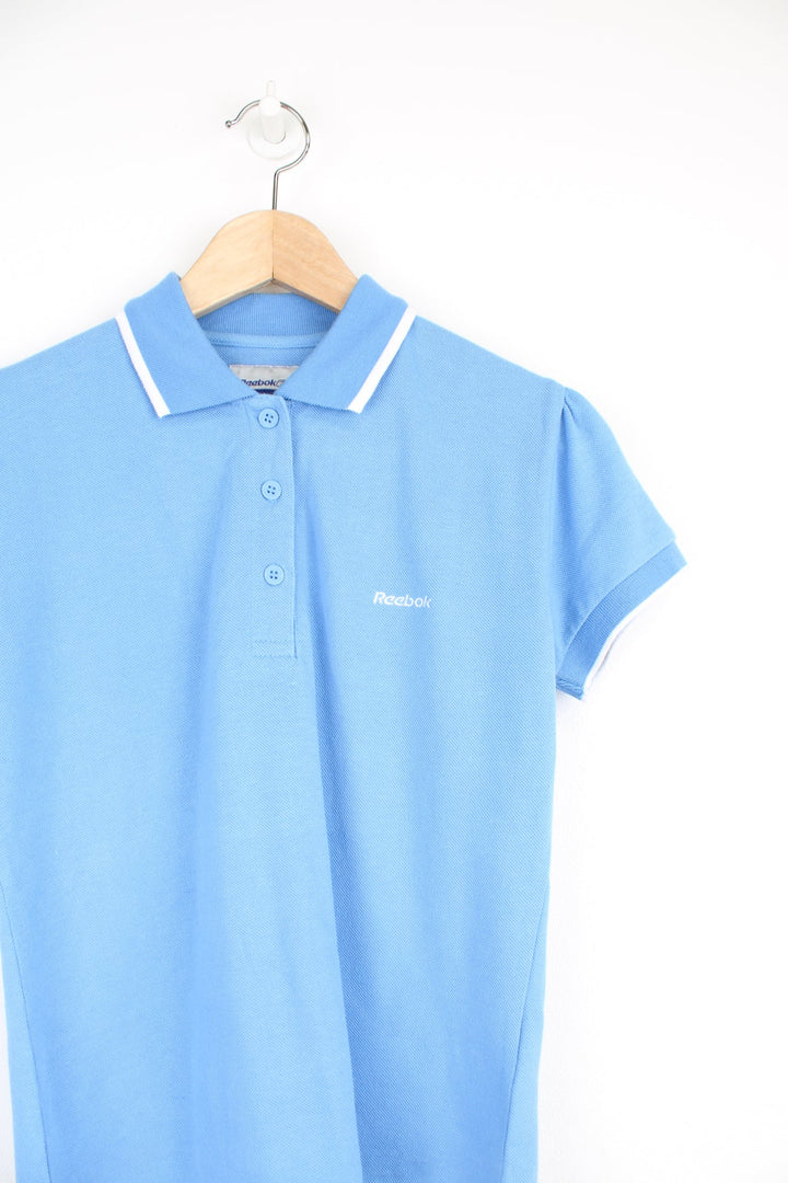 Vintage women's baby blue polo shirt by Reebok, features embroidered logo on the chest and white trim on the collar and sleeves