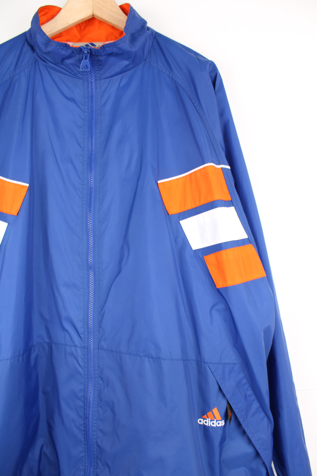 Adidas Windbreaker in a blue, white and orange colourway, zip up with side pockets, and has the logo embroidered on the front and left sleeve.