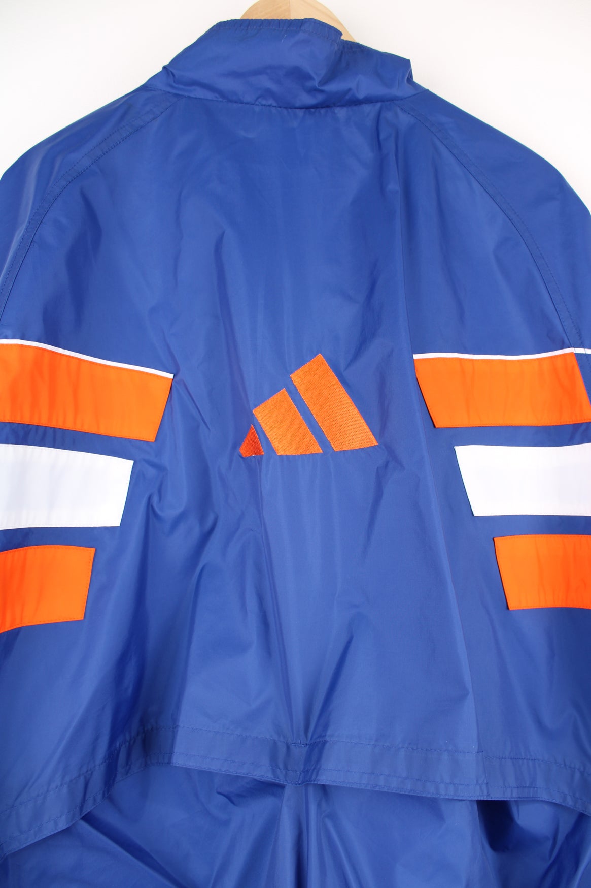 Adidas Windbreaker in a blue, white and orange colourway, zip up with side pockets, and has the logo embroidered on the front and left sleeve.