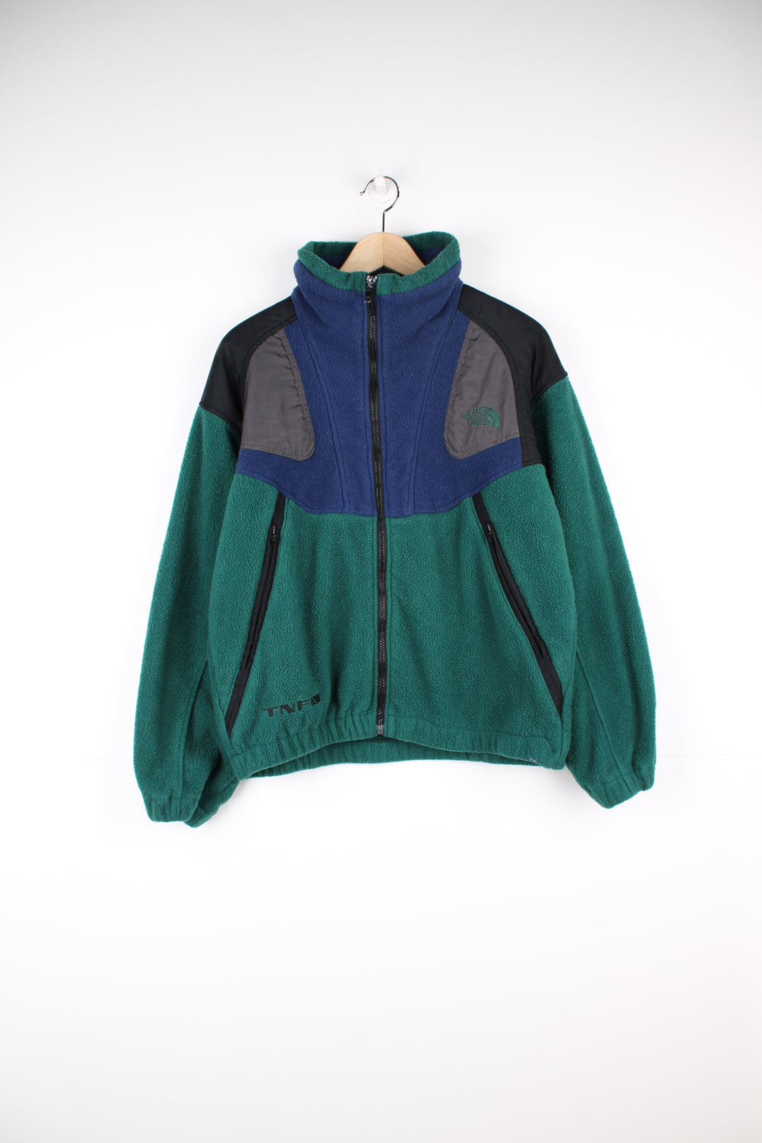 The North Face Fleece in a green, blue and black colourway, zip up with side pockets, and has the logo embroidered on the front and back.