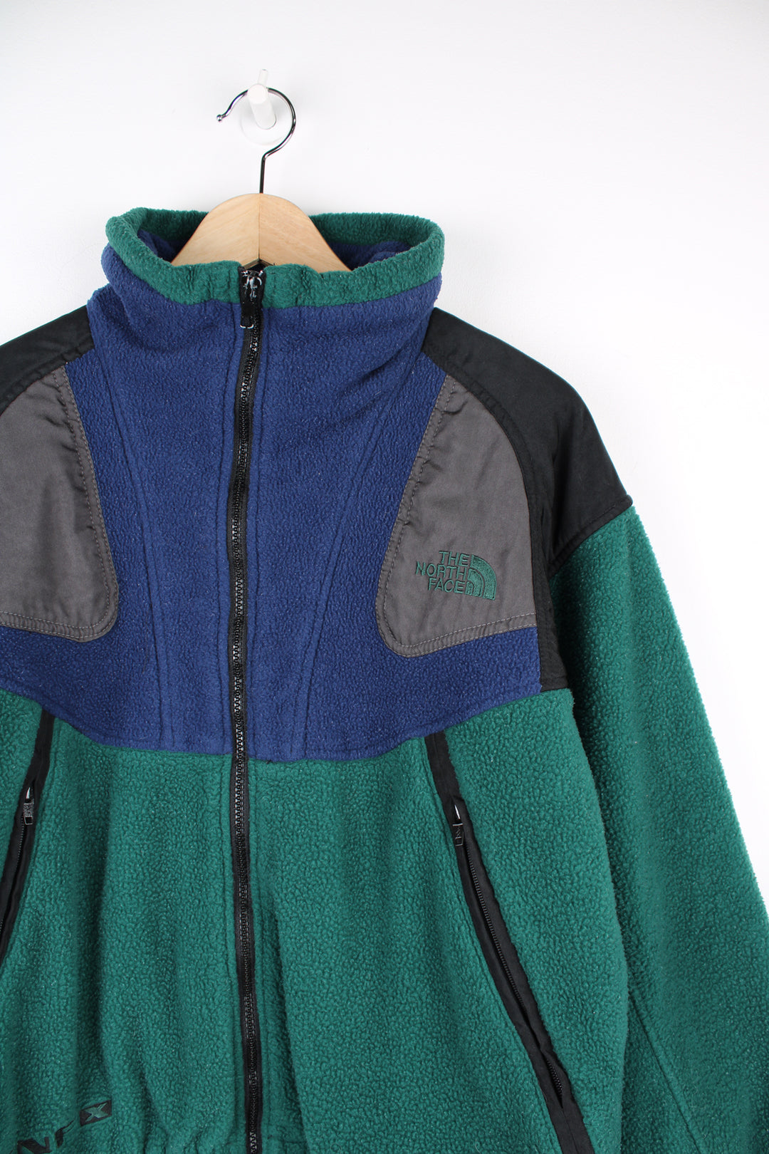 The North Face Fleece in a green, blue and black colourway, zip up with side pockets, and has the logo embroidered on the front and back.