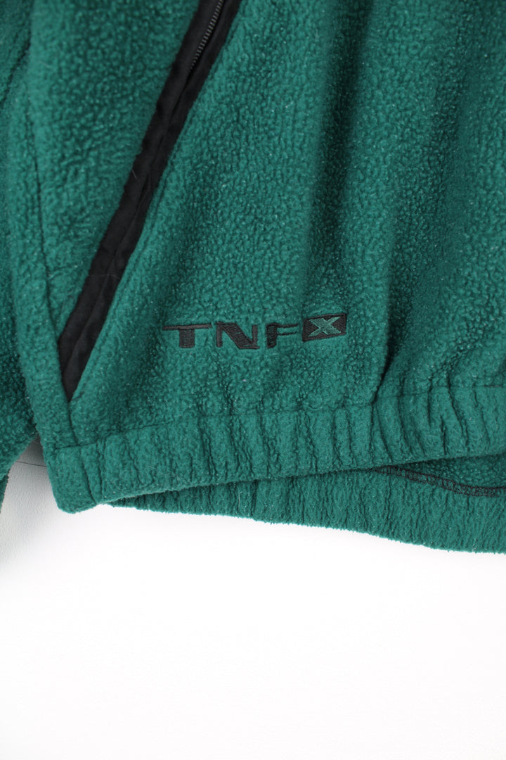 The North Face Fleece in a green, blue and black colourway, zip up with side pockets, and has the logo embroidered on the front and back.