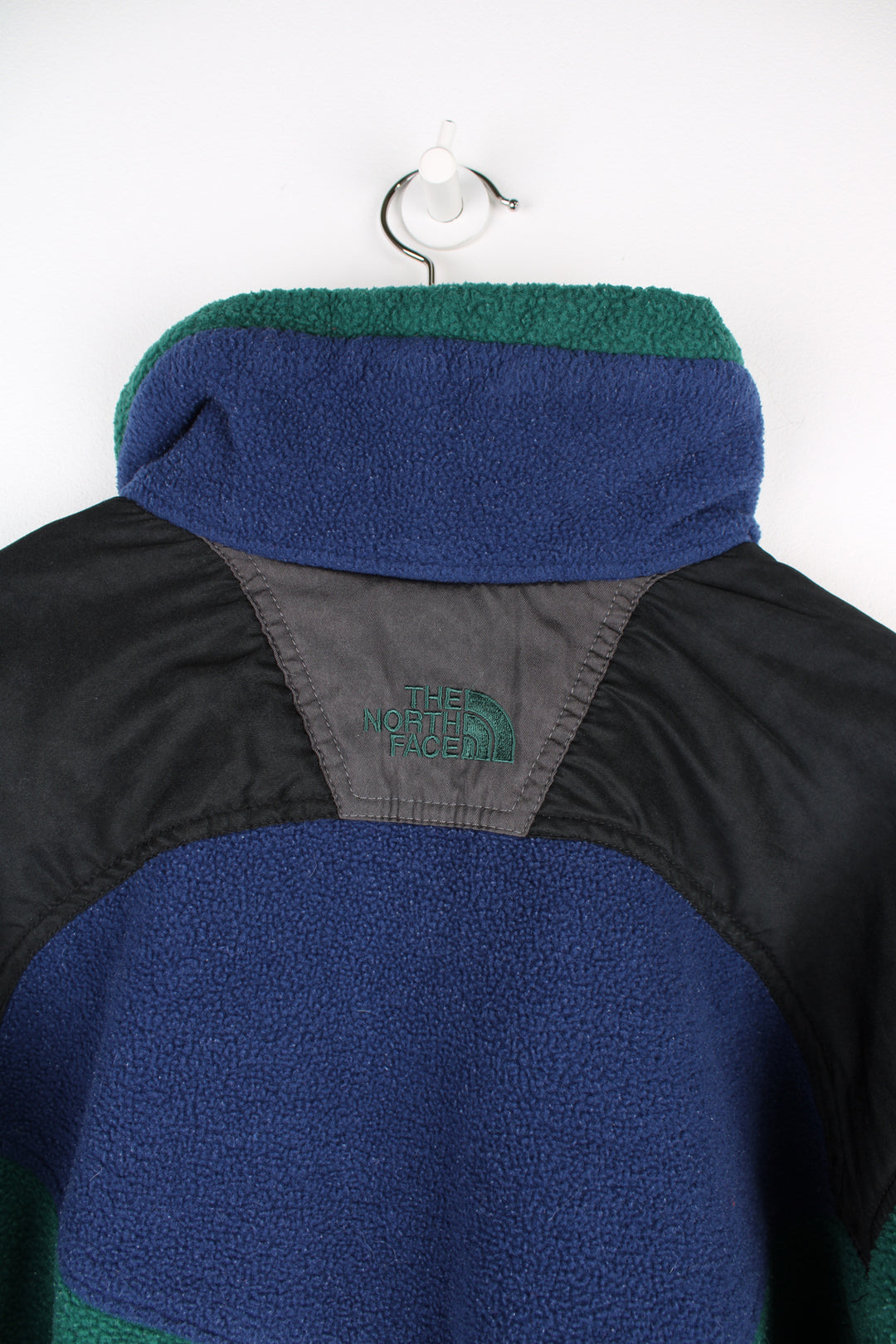 The North Face Fleece in a green, blue and black colourway, zip up with side pockets, and has the logo embroidered on the front and back.