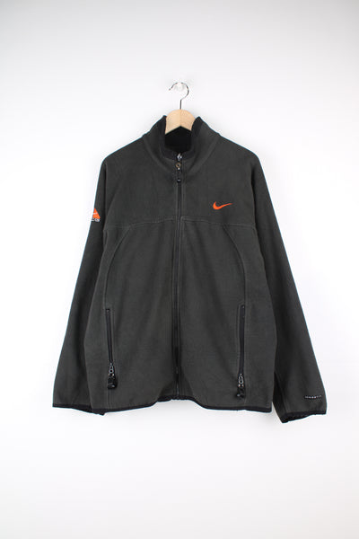 Nike ACG Fleece in a grey colourway, zip up with side pockets, air vent zips under arm pits, and has the swoosh logo embroidered on the front, back and right sleeve.