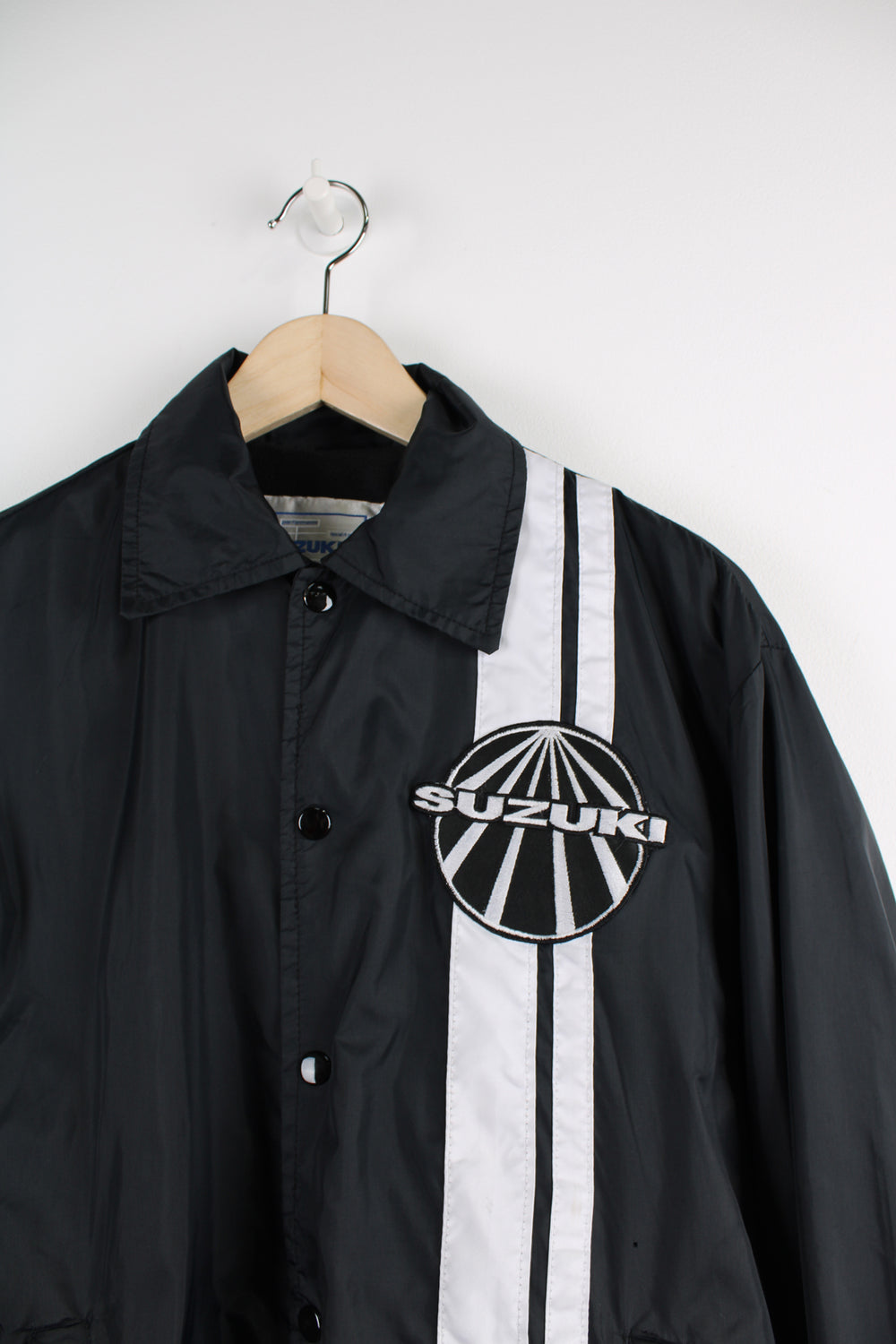 Vintage all black, button up nylon coach jacket by Suzuki. Features embroidered badge on the chest  