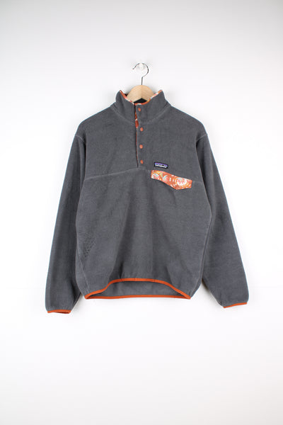 Patagonia Synchilla Fleece in a grey colourway with orange tropical floral print on the collar and chest pocket, quarter button up, and has the logo embroidered on the front.