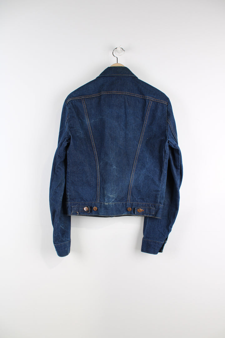 Vintage Wrangler Denim Jacket in a blue colourway with brown cross stitching, button up, multiple pockets, and has logo embroidered on the chest.