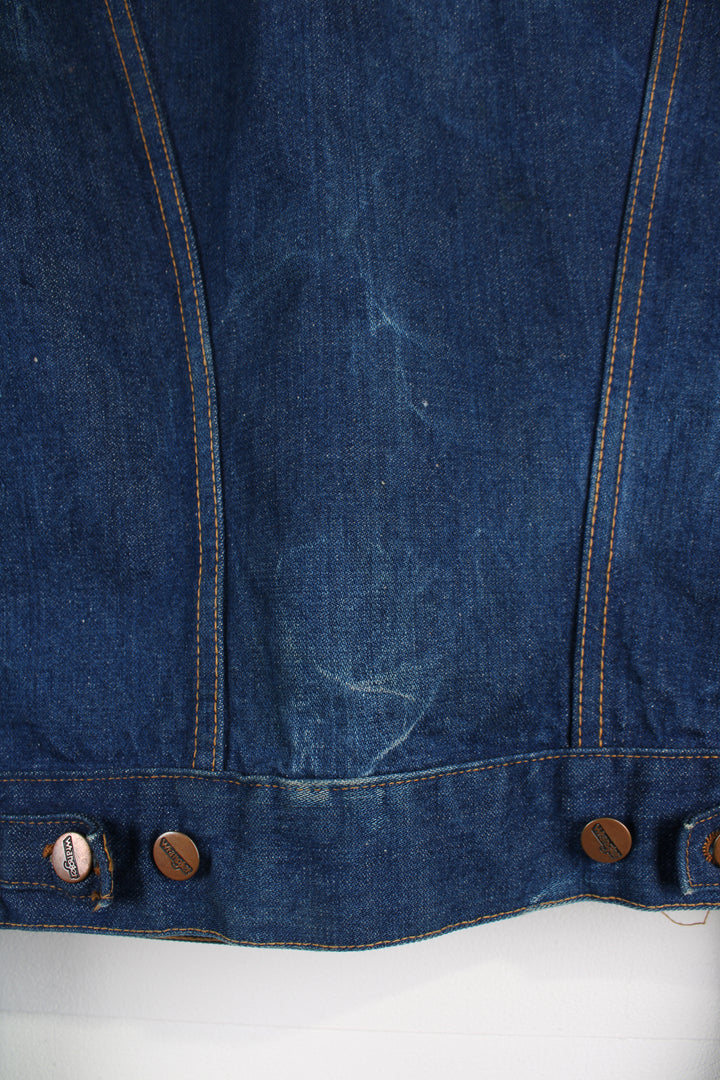 Vintage Wrangler Denim Jacket in a blue colourway with brown cross stitching, button up, multiple pockets, and has logo embroidered on the chest.