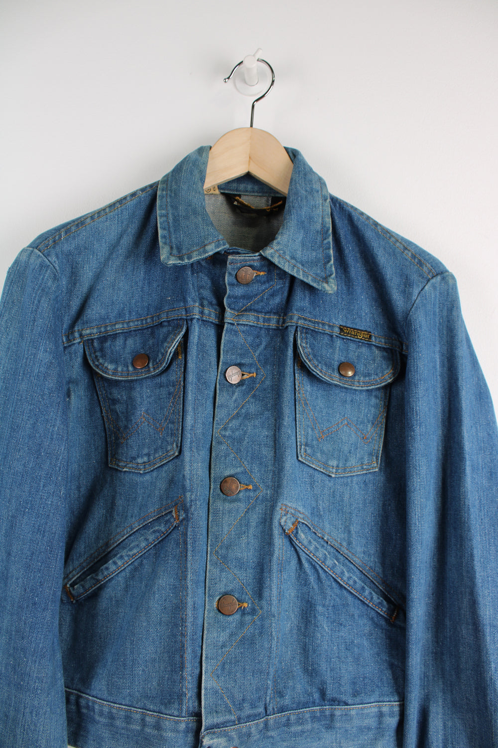 Vintage Wrangler Denim Jacket in a blue colourway with brown cross stitching throughout, button up, multiple pockets, and has logo embroidered on the chest.