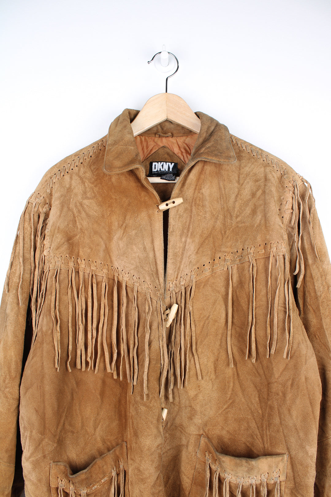 Vintage 90's DKNY fringe jacket. Tan suede jacket with fringe and whip stitch detail. The jacket is fully lined and closes with wooden toggle style buttons down the front. Fair condition - The jacket is discoloured in places and is missing some tassels on the shoulder and pocket. Size in Label: Womens L 12 - 14 