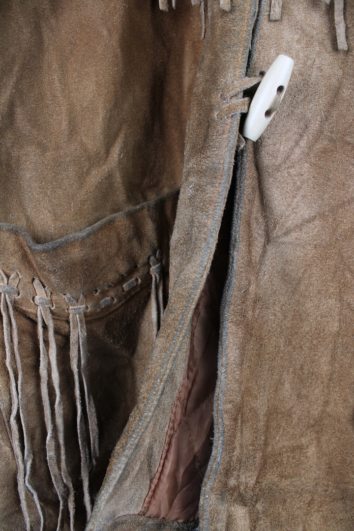 Vintage 90's DKNY fringe jacket. Tan suede jacket with fringe and whip stitch detail. The jacket is fully lined and closes with wooden toggle style buttons down the front. Fair condition - The jacket is discoloured in places and is missing some tassels on the shoulder and pocket. Size in Label: Womens L 12 - 14 