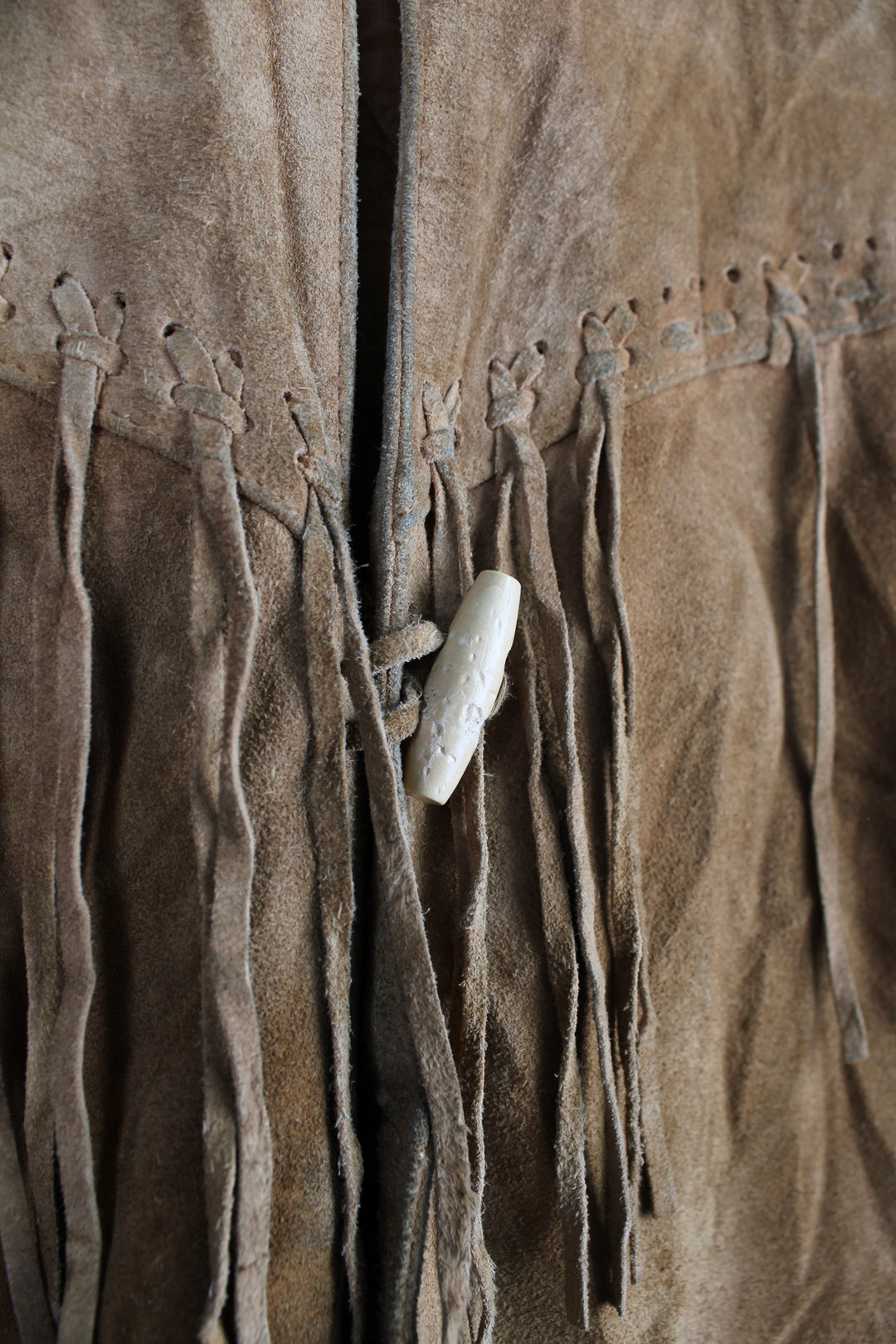 Vintage 90's DKNY fringe jacket. Tan suede jacket with fringe and whip stitch detail. The jacket is fully lined and closes with wooden toggle style buttons down the front. Fair condition - The jacket is discoloured in places and is missing some tassels on the shoulder and pocket. Size in Label: Womens L 12 - 14 